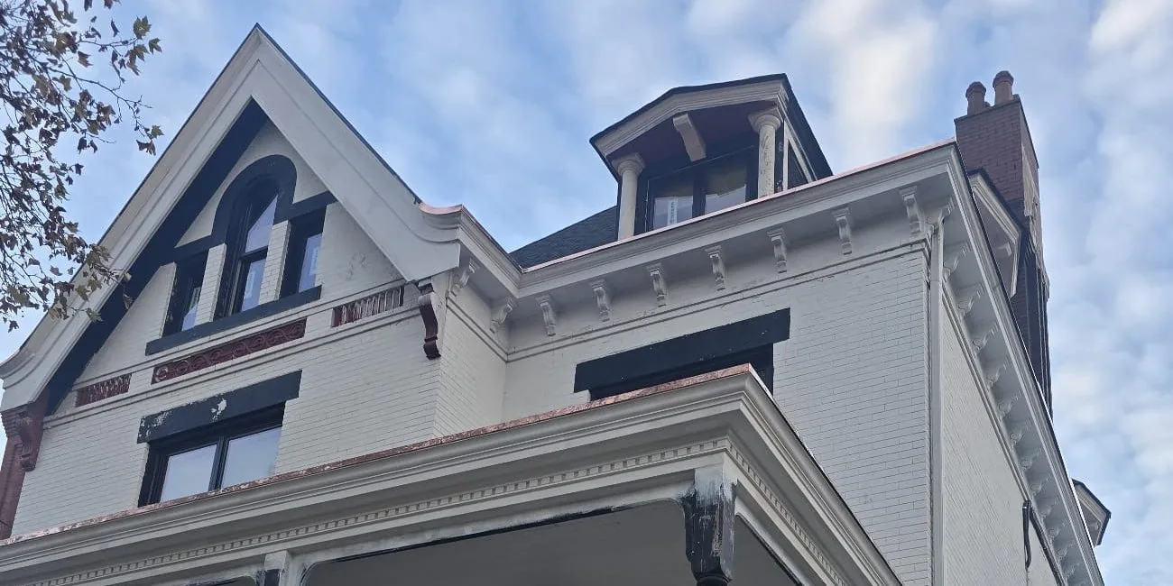 The roof and siding of a large brick house against a blue sky
