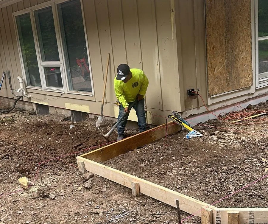 A crew member digging and forming footings beside a house