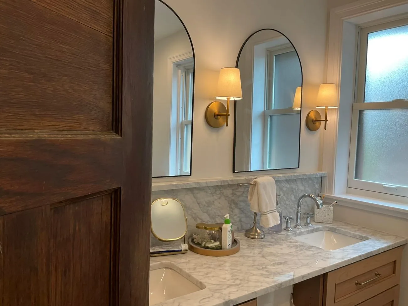 A bathroom vanity in wood with two arched mirrors and wall sconces